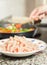 Closeup of raw chiken dish and female cooking in a pan in the ba