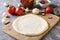 Closeup of raw dough prepared for pizza on the wooden board and different classic ingredients for it on the grey kitchen table