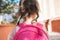 Closeup rear view portrait of cute little girl preschooler posing outdoor with pink backpack against blurred building. Happy kid