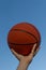 Closeup of red basketball in a man's hands with clear blue sky background