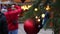 Closeup of a red Christmas ball hang on a natural New Year tree on a city fair, crowd of people walking on a festive city square o