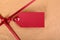 Closeup red gift tag and ribbon, brown parcel wrapping paper background