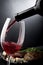 Closeup of red wine pouring into a glass in front of plate with cheese and meat