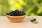 Closeup ripe black mulberries in wicker basket on the table on green leaves background.