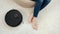 Closeup of robot vacuum cleaner doing housework and cleanup around woman relaxing in chair at living room. Concept of