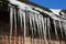 Closeup of row isolated sharp icicles hanging from reed roof of german timbered house on sunny day