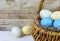 Closeup of a rustic Easter basket with brown paper grass and blue, green and yellow spotted or speckled eggs on a whitewashed