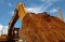 Closeup rusty metal bucket of old backhoe parked at construction site against blue sky. Excavating machine. Earth moving machine.