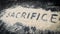 Closeup of SACRIFICE word written on white sand