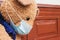 Closeup of sad teddy bear toy wearing disposable medical protective face mask sitting on vintage brown bench. Stay at