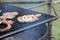 Closeup of sausages and beef grilling on an outdoor grill in a park