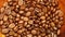 Closeup scene of coffee beans falling into a pile of coffee beans.