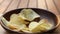 Closeup scene of potato chips fall into a wooden plate on the table