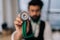 Closeup selective focus of blurred Indian male cardiologist in glasses holding stethoscope on hand for listening check
