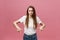 Closeup of serious strict young woman wears white shirt looks stressed and pointing up with finger isolated over pink