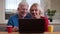 Closeup shoot of aged happy couple having a video call on the laptop with cups with tea on the desk and waving hi