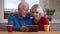 Closeup shoot of aged happy couple having a video call the tablet with cups with tea on the desk indoors in a cozy