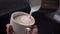 Closeup shoot of barista pouring milk into a steaming coffee in a cup using the silver pitcher preparing cappuccino