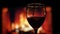 Closeup shoot of red wine being poured into the empty glass with cozy warm fireplace with flames on the background