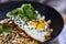 Closeup shot of a bibimbap dish with fresh herbs in a black bowl