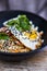 Closeup shot of a bibimbap dish with fresh herbs in a black bowl