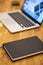 Closeup shot of a black notebook on a wooden table with a laptop on a blurry background