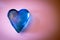 Closeup shot of a blue crystal heart pebble on a pink surface