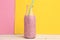 Closeup shot of a bottle of strawberry milkshake on a pink and yellow background