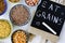 Closeup shot of bowls of healthy grains on a white background with text on a chalkboard