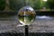 Closeup shot of a clear round glass ball reflecting a stone water fountain