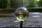 Closeup shot of a clear round glass ball reflecting a stone water fountain