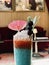 Closeup shot of a colorful beverage with a pink umbrella, cherries on a stick, and some leaves in it