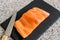 Closeup shot of a delicious piece of salmon on a black board next to a  knife