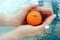 Closeup shot of a female hand holding a wrinkled orange a swimming pool