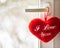 Closeup shot of a fluffy red heart plush toy with text [I Love You] hanging on a white door handle