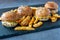 Closeup shot of four delicious sliders and a pile of crispy  fries on a slate plate