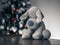 Closeup shot of a gray stuffed dog on a brown surface on the background of a Christmas tree