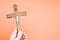 Closeup shot of a hand holding a wooden crucifixion of Christ cross on a pastel peach background