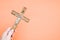 Closeup shot of a hand holding  wooden crucifixion of Christ cross on a pastel peach background