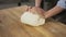 Closeup shot of hands of senior bakery chef applying flour on dough, aged man kneading dough, making bread using