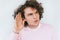 Closeup shot of handsome eavesdropping male with curly hair placing hand on ear asking someone to speak up, isolated over white