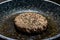 Closeup shot of a homemade beef burger patty in an oily frying pan