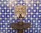Closeup shot of an interesting fountain with a square face sculpture on a blue-tiled wall