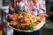 Closeup shot of a lady holding a serving of barbeque with fries, onion, tomato, lettuce, orange