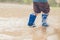 Closeup shot of the legs of a boy in blue rubber boots splashing in a puddle