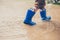 Closeup shot of the legs of a boy in blue rubber boots splashing in a puddle