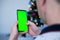 Closeup shot of man  hand using mobile phone with Green screen against the backdrop of a Christmas tree. Finger swiping up and