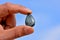 Closeup shot of a man holding a teardrop shape stone with a clear blue sky in the background