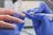 Closeup shot of manicurist in blue rubber gloves cleans cuticle on female nails using a milling cutter for manicure