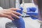 Closeup shot of manicurist in blue rubber gloves and medical mask removes cuticle on female nails using manicure tools